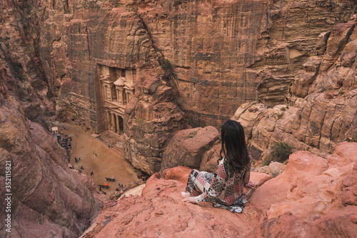 A woman traveller sitting at viewpoint of Petra ancient city looking at the Treasury or Al-khazneh, Jordan, Arab