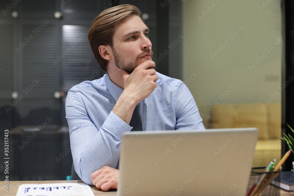 Thoughtful modern business man working using laptop while sitting in the office. Thoughtful modern business man working using laptop while sitting in the office.