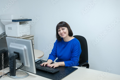 Office  brunette woman in blue dress smiling at her Desk