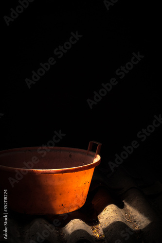 Old worn red bucket standing in a foggy environment on the attic. Red bucket lit by a ray of light from the attic window.