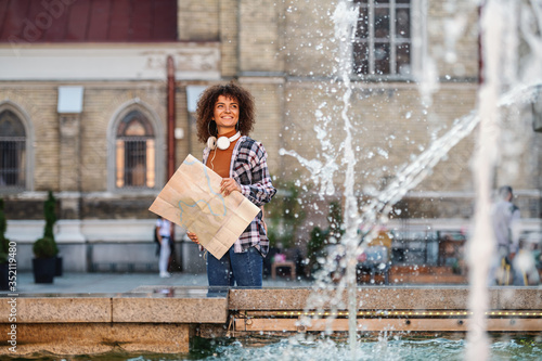 Young attractive mixed race woman behind fountain, looking at it and holding map.