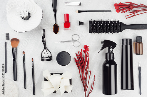 Stylish glossy black cosmetic products and mack up accessories with red twig and nail polish on soft light white wooden background, top view, pattern. photo