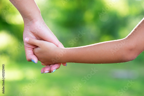Mother leads kid, summer forest outdoor. Trust, family, protection and help concept. Female and child's hands closeup against the background of summer greenery. Parent walks with daughter in park © Khorzhevska