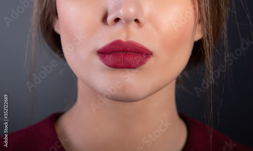 Sexy lips with deep red lipstick of young woman over gray background. Botton half of female face with blank expressions