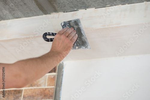 Putty knife in male hand. Hand workю Worker putsty plasterboard ceiling in new appartment. Repairman works with plasterboard, plastering dry-stone wall, home improvement. Man makes repairs at house.