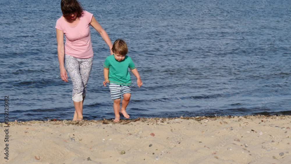 Mom playing with little child boy on seashore. Adult woman and her son enjoying summer day on beach. Family vacation at sea. Slow motion Mom playing with little child boy on seashore. Adult woman and her son enjoying summer day on beach. Family vacation at sea. Slow motion