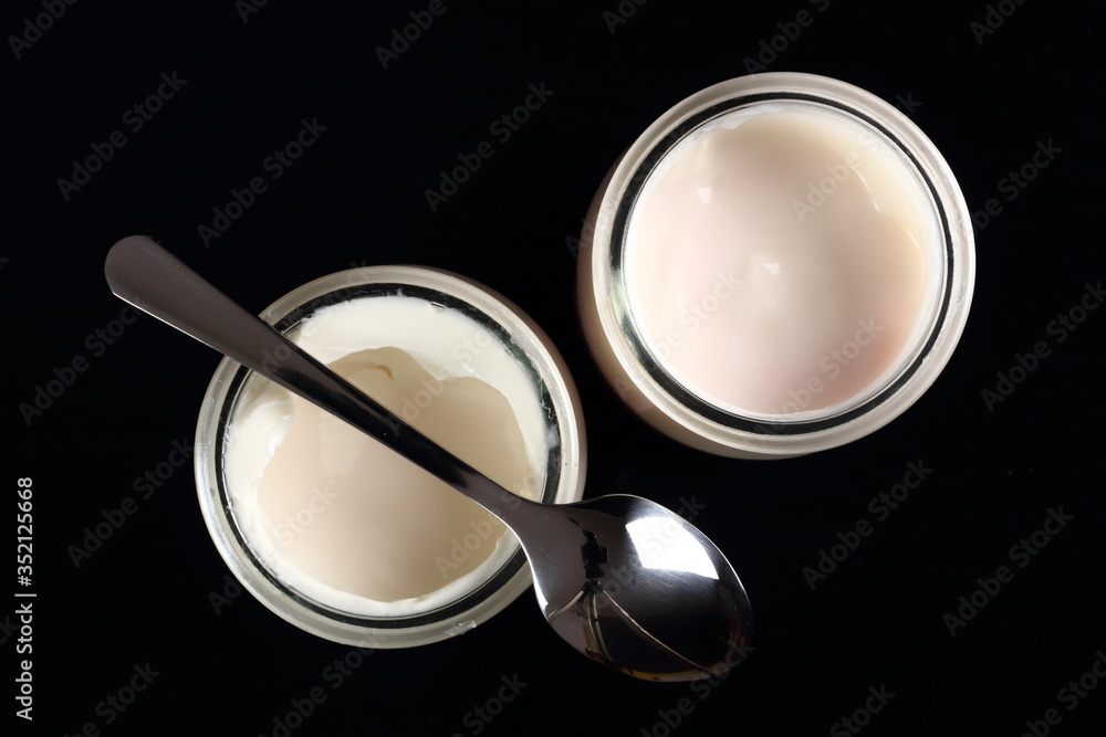 Yogurt in open small glass jar with spoon at black background. D Yogurt in open small glass jar with spoon at black background. D