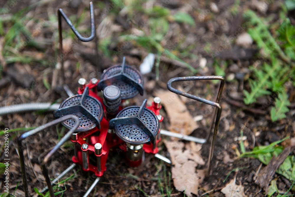 tourist gas burner of red color on the ground with green grass in natural conditions ready to use tourist gas burner of red color on the ground with green grass in natural conditions ready to use