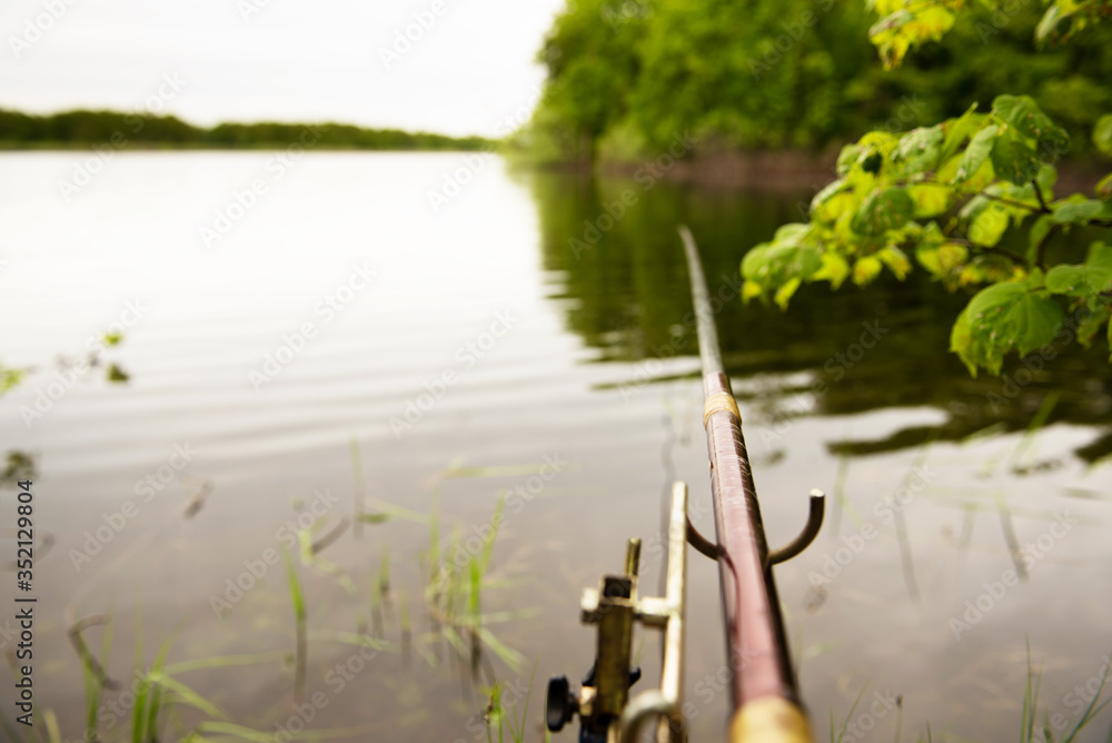 fishing background. Fishing rod mounted on a stand against a background of lake and trees fishing background. Fishing rod mounted on a stand against a background of lake and trees