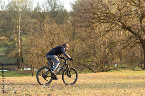 Sports brutal bearded guy on a modern mountain bike. Cyclist on the green hills in the spring.