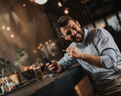 Man drinking beer, smoking cigarette and looking at mobile phone at the pub