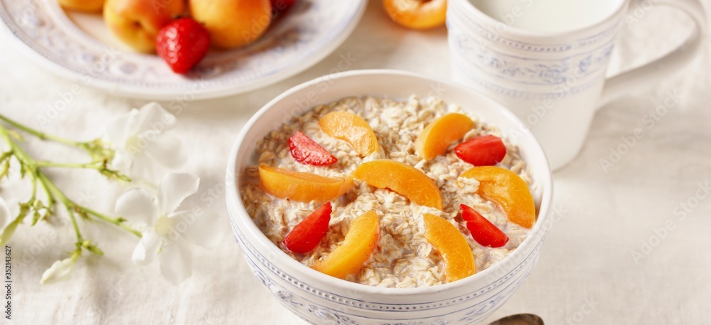 breakfast with oatmeal and fruit, apricot and strawberries with milk. Summer season, fresh fruits, copy space breakfast with oatmeal and fruit, apricot and strawberries with milk. Summer season, fresh fruits, copy space