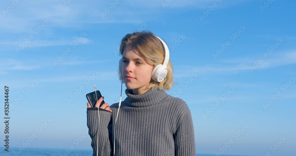 Young handsome female listen to music with headphones outdoor on the beach against sunny blue sky	