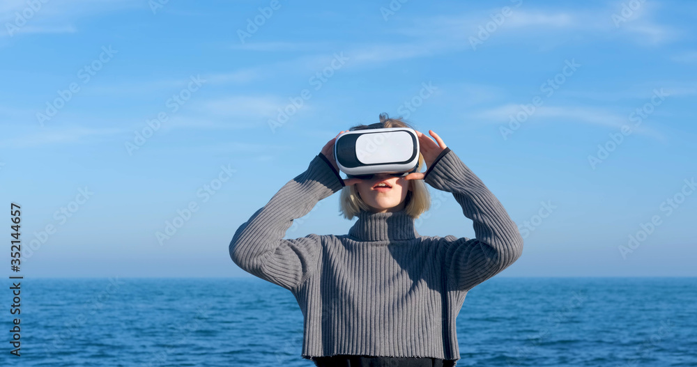 Obraz premium Young handsome female with virtual reality glasses outdoor on the beach against sunny blue sky