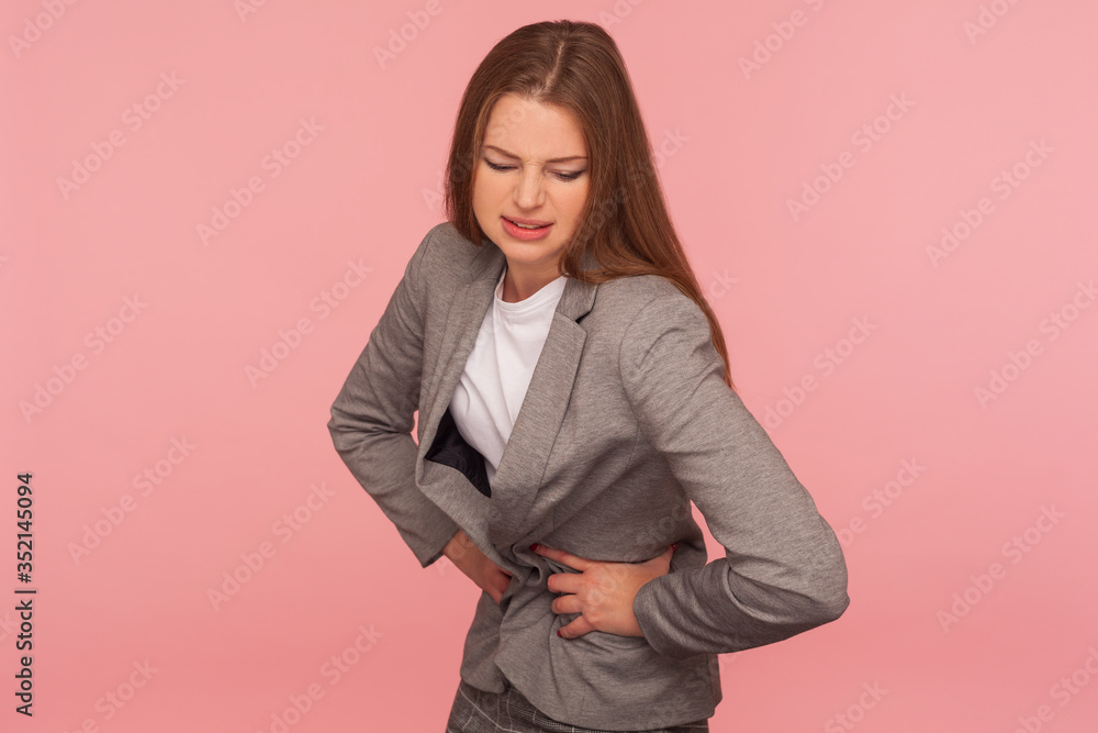 Stomachache. Portrait of unhealthy young woman in business suit feeling discomfort in belly, suffering abdominal pain, heartburn or gastritis, constipation symptoms. indoor studio shot, isolated Stomachache. Portrait of unhealthy young woman in business suit feeling discomfort in belly, suffering abdominal pain, heartburn or gastritis, constipation symptoms. indoor studio shot, isolated