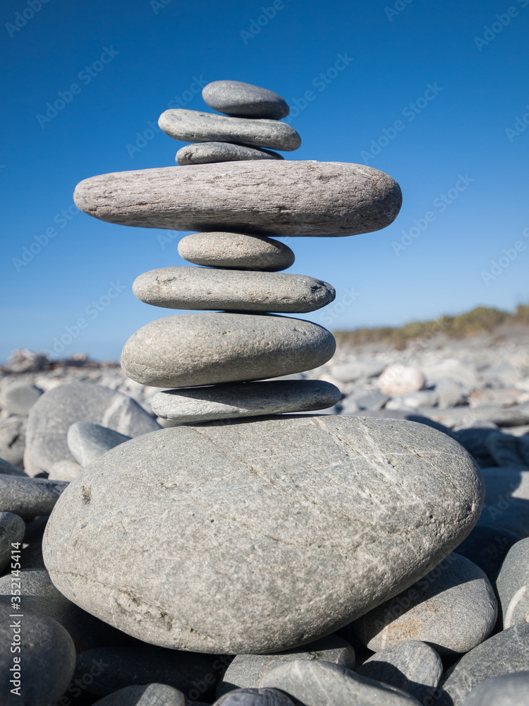 A beautiful rock and beach stone pebble stack on a pebble beach with a vivid blue sky background. Zen, mindfulness, meditation and relaxation. Stones have unique healing properties. A beautiful rock and beach stone pebble stack on a pebble beach with a vivid blue sky background. Zen, mindfulness, meditation and relaxation. Stones have unique healing properties.