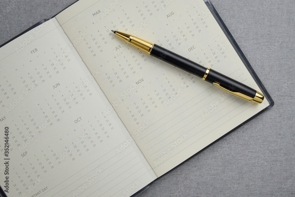 Black and gold fountain pen placed on calendar notebook on gray cement texture background. Task management concept. Black and gold fountain pen placed on calendar notebook on gray cement texture background. Task management concept.