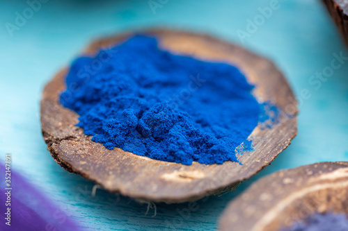 Blue food coloring powder in a coconut plate on a cyan table top. Close up of a blue powder.