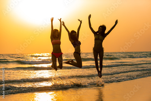 Silhouette group of happy young beautiful Asian women in bikini swimwear playing and jumping together on tropical beach at sunset. Three sexy girls friends having fun in summer holiday vacation travel