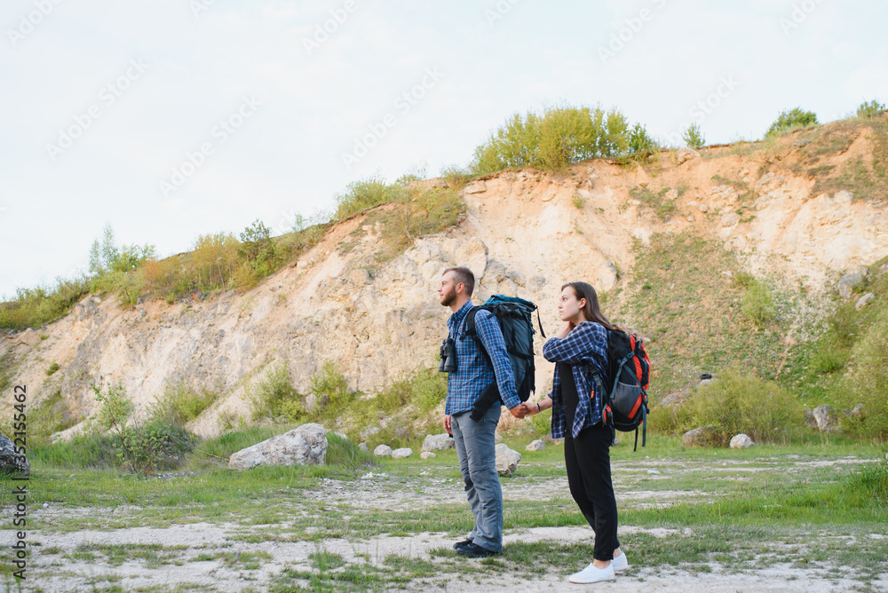 Beautiful couple of a travelers are searching way on location map while standing on high hill in sunny day, male and female hikers are walking together in mountains during long awaiting summer weekend