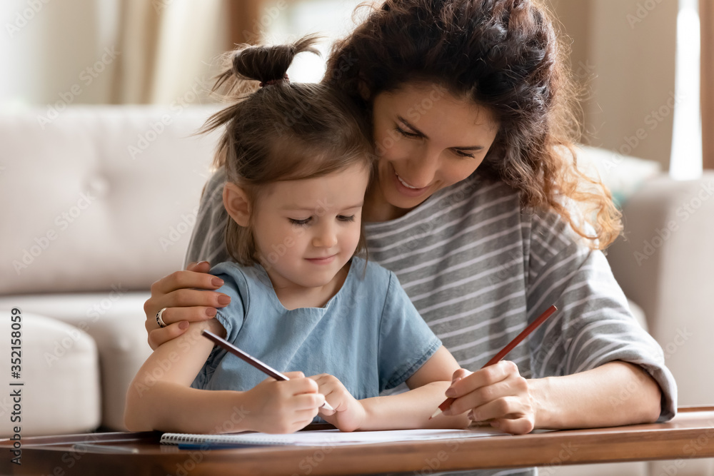 Smiling mother and cute little daughter drawing with colorful pencils close up, sitting at desk in living room, loving caring mum and adorable preschool girl child having fun, coloring together Smiling mother and cute little daughter drawing with colorful pencils close up, sitting at desk in living room, loving caring mum and adorable preschool girl child having fun, coloring together