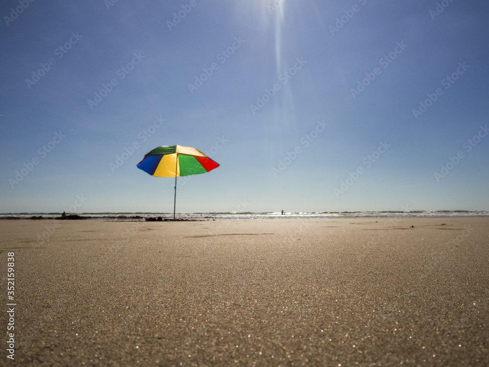 red green and blue sum shade umbrella on a sandy beach with ocean in the background 