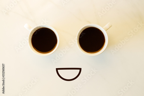 Two cups of coffees arranged as human face with line showing emotion. Smile