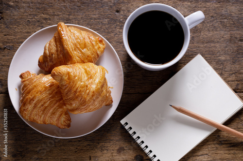 cup of hot coffee  with croissant on dark wooden background.  Working at home concept.