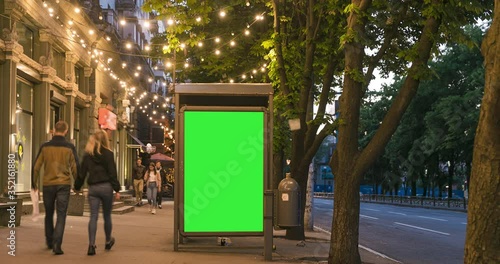 City street Billboard stand with chroma key green screen. Time lapse with commuters, people and cars. Space for text or copy. Warm lights atmosphere for advertising video