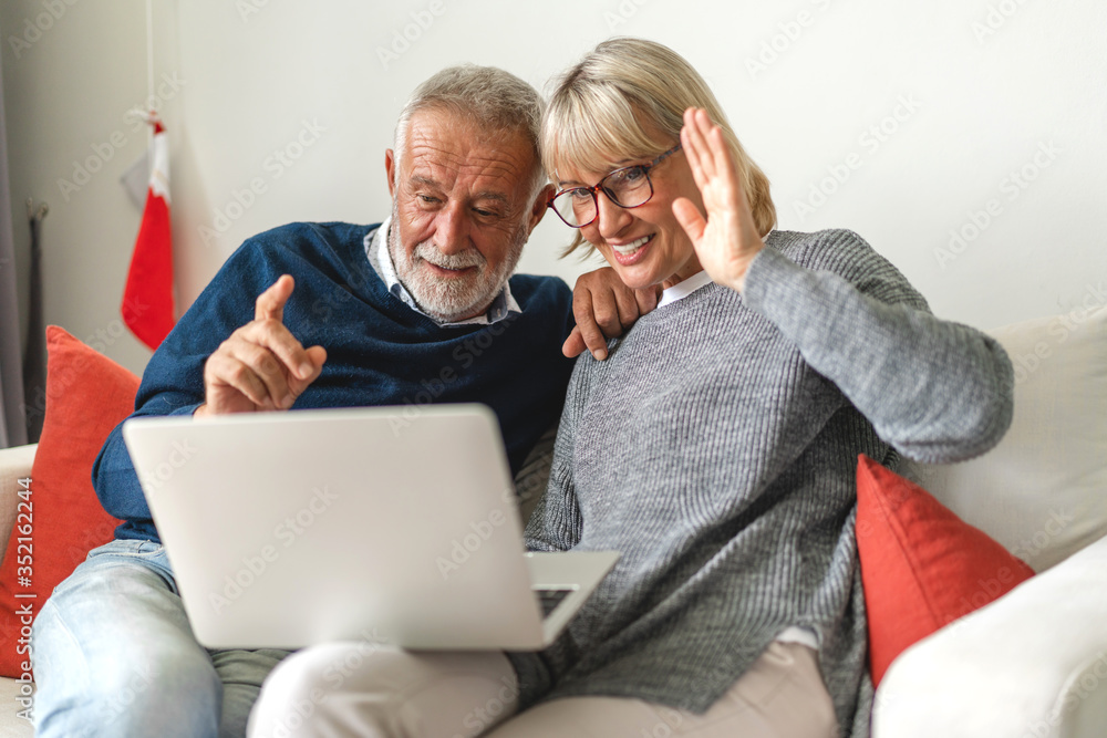 Senior couple family having good time using laptop computer together.Happy elderly husband and wife checking social media and reading news or shopping online while sitting on sofa at home.Retirement 
