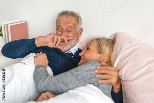 Senior happy couple relaxing and talking together lying on bed in bedroom at home.Elderly husband and wife looking at camara.Retirement couple concept