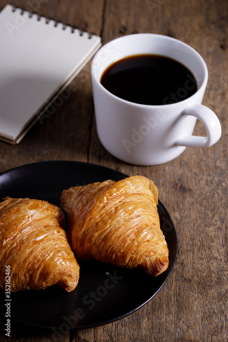 cup of hot coffee  with croissant on dark wooden background.  Working at home concept.