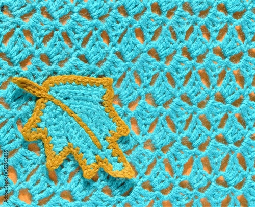 Crocheted teal leaf and crocheted pattern sample on orange background.