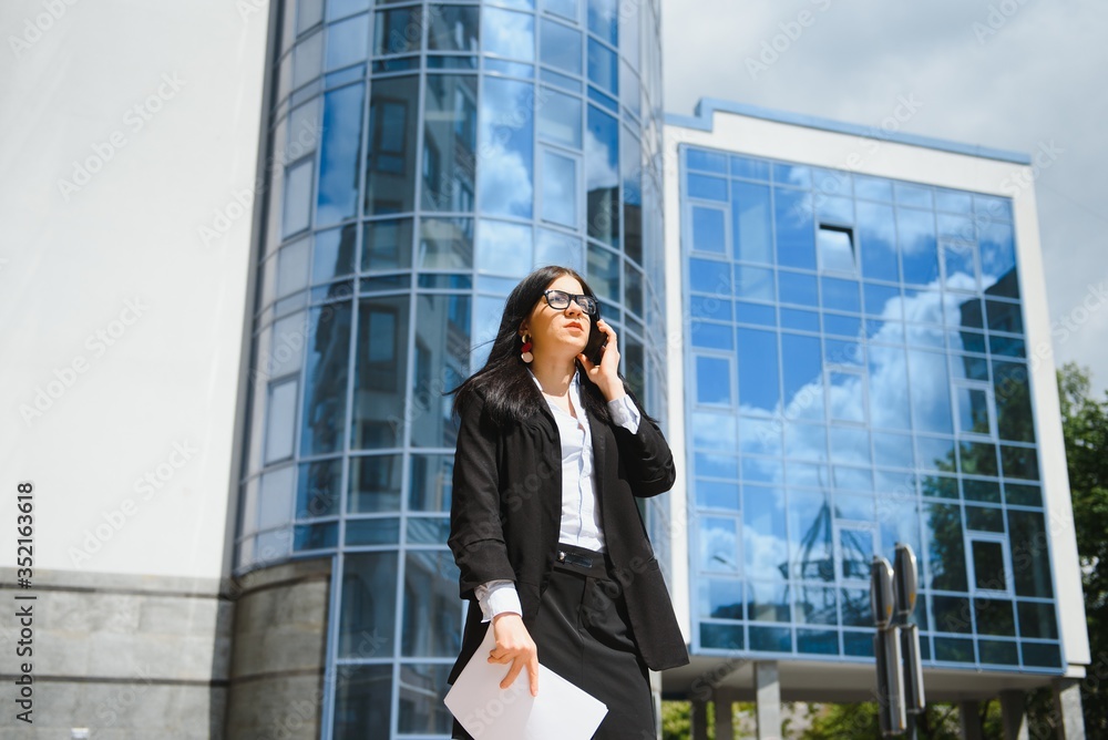 Successful businesswoman or entrepreneur taking notes and talking on cellphone while walking outdoor. City business woman working. Successful businesswoman or entrepreneur taking notes and talking on cellphone while walking outdoor. City business woman working.