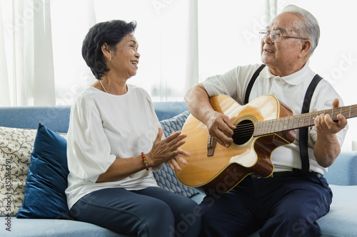 Portrait of an elderly couple enjoying playing the guitar in their own home. They have a smiling and happy face. Activity concept of retirement age