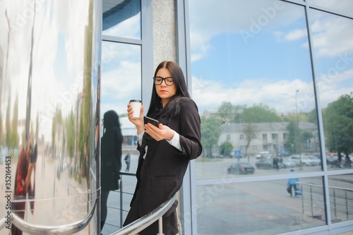 Portrait of successful business woman going to work with coffee walking near office building on city street.