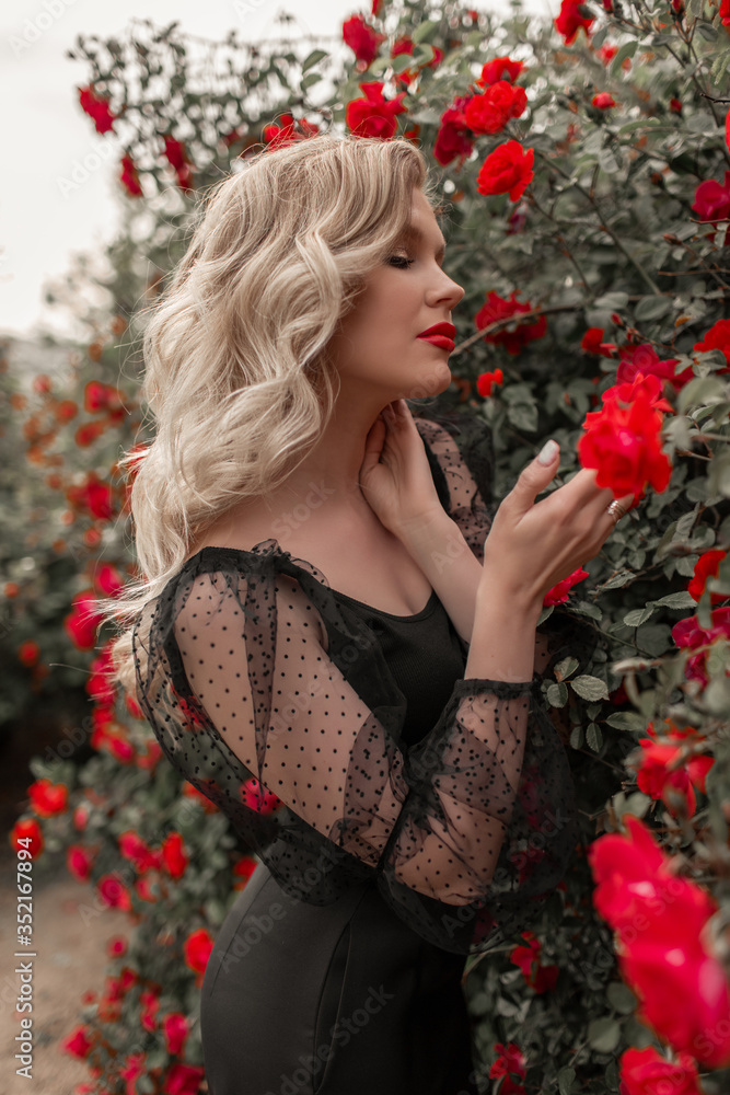 Portrait of young beautiful blonde woman in spring garden with red blossom roses.