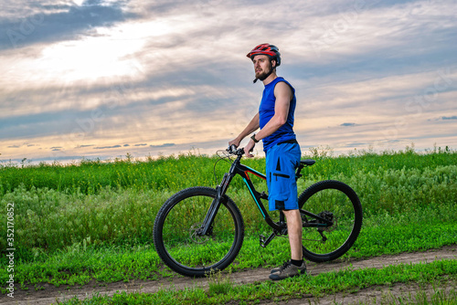 A young man in a helmet with a bicycle standing near the field.