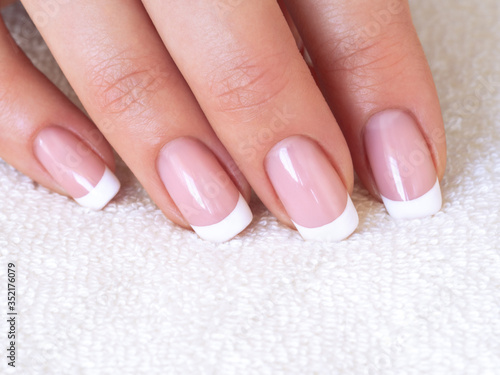 Female well-groomed fingers with french classic manicure on white terry towel, close up, selected focus.