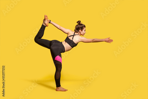 Dancer pose. Slim woman with hair bun in tight sportswear practicing yoga, doing Natarajasana exercise on one leg, stretching muscles and balancing. full length studio shot, sport workouts isolated