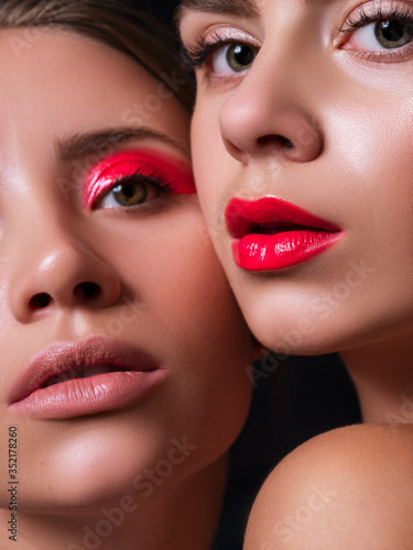 Two women together close to each other with red lips and eye. Close up creative beauty cosmetics concept. Fresh flawless skin. Portrat on dark background