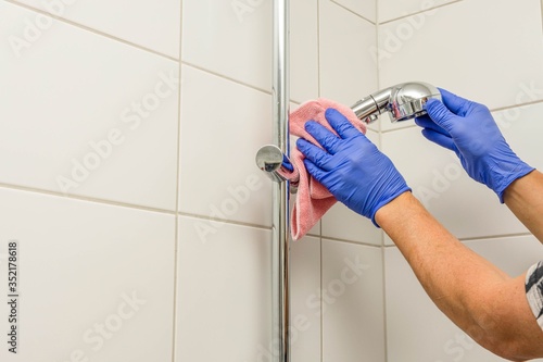 Close up view of man in blue gloves cleaning shower faucet. Cleaning hygien concept background. 