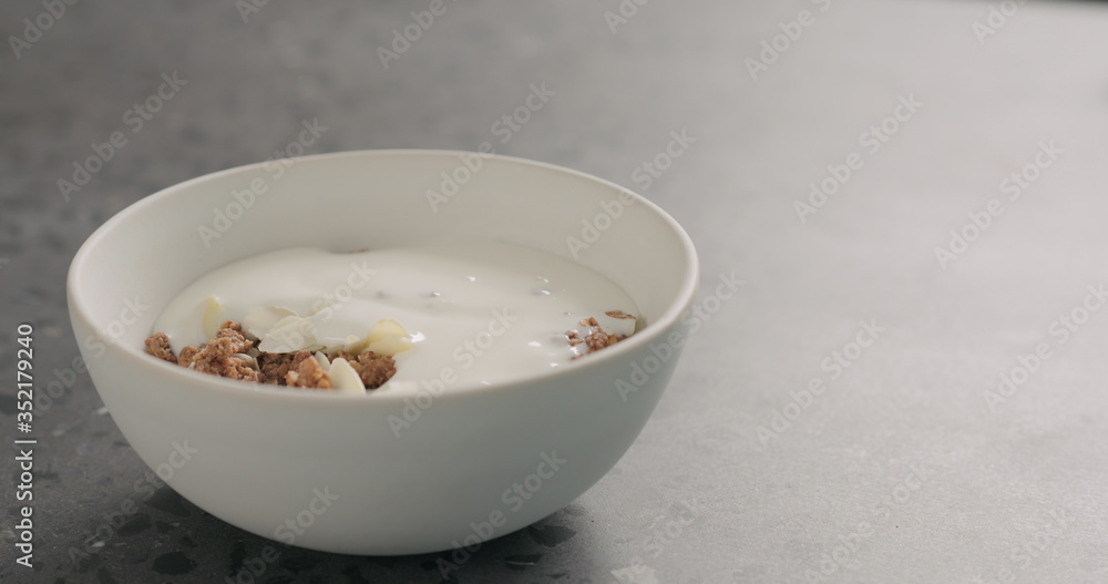 yogurt over chocolate granola in white bowl on terrazzo surface yogurt over chocolate granola in white bowl on terrazzo surface