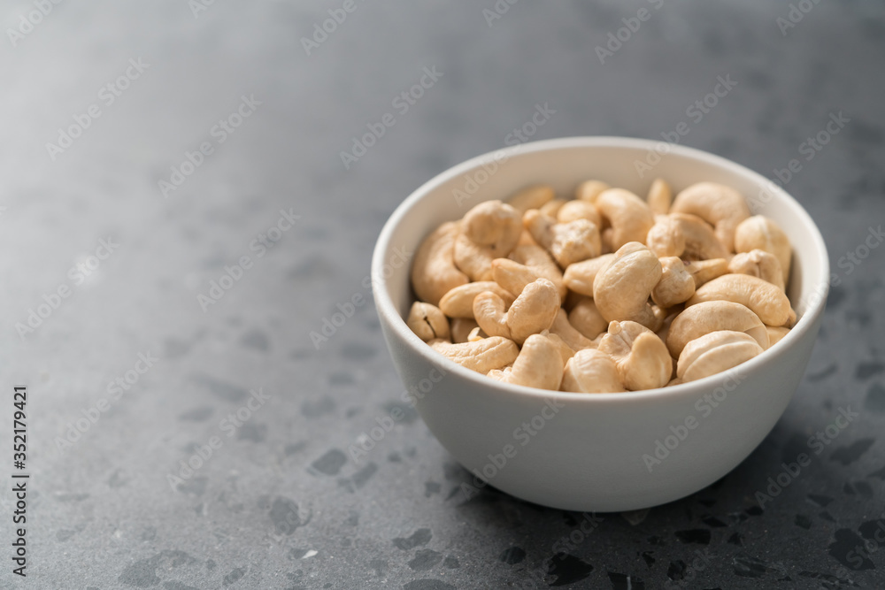 Dry cashew nuts in white bowl on concrete background with copy space Dry cashew nuts in white bowl on concrete background with copy space