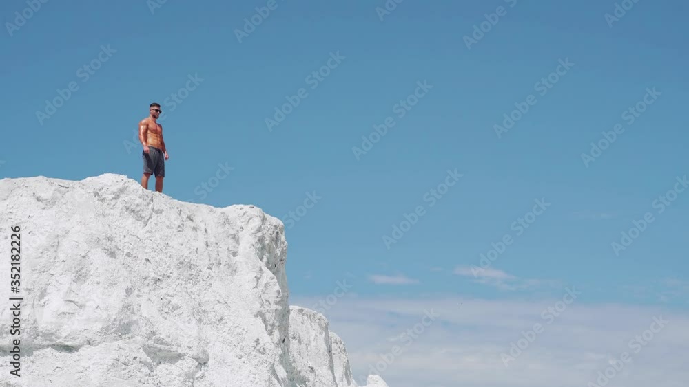 The winner man runs to the top of the mountain. A shirtless bodybuilder stands on a mountain against a blue sky. The winner man runs to the top of the mountain. A shirtless bodybuilder stands on a mountain against a blue sky.