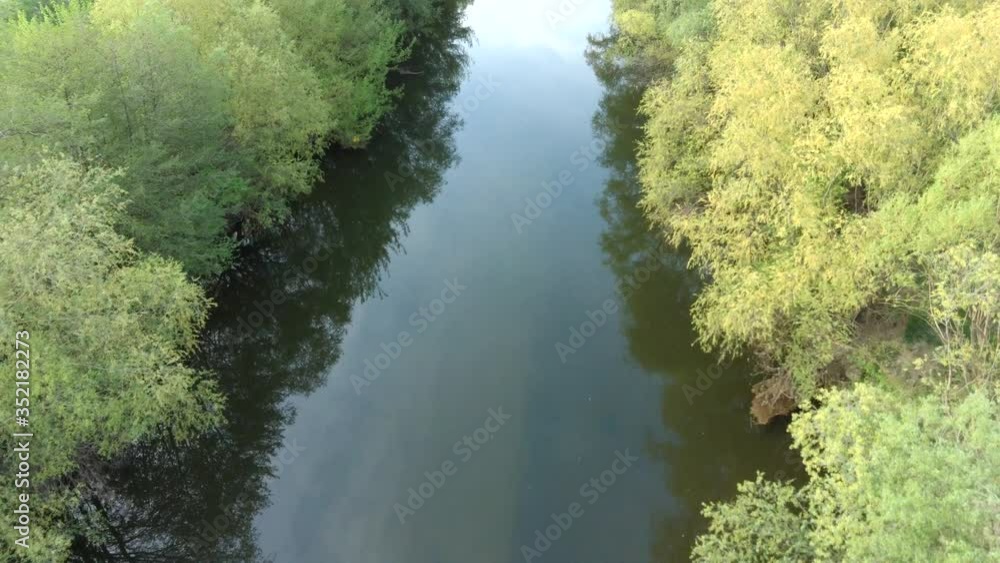 Spring low level flight above river with broadleaf trees on both banks Spring low level flight above river with broadleaf trees on both banks