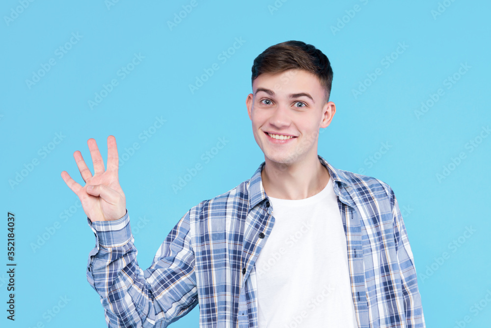 Cheerful smiling guy dressed in white t-shirt, checkered shirt on blue background. Young man is showing with fingers number four, percents, discount. Male gesturing. Emotional portrait concept. Cheerful smiling guy dressed in white t-shirt, checkered shirt on blue background. Young man is showing with fingers number four, percents, discount. Male gesturing. Emotional portrait concept.