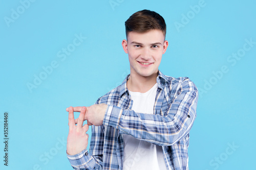 Smiling guy student dressed in white t-shirt, checkered shirt is standing on blue background. Young man blogger, streamer is showing with fingers hashtag sign. Social media user concept.