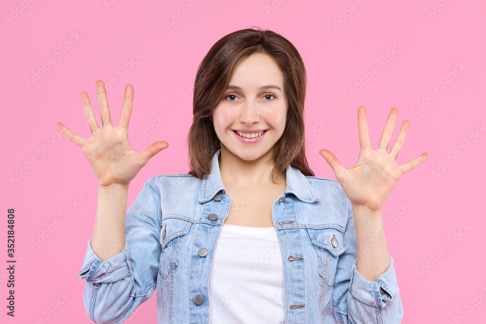 Cheerful smiling girl dressed in white t-shirt, denim jacket on pink background. Young woman is showing with fingers number ten, percents, discount. Female gesturing. Emotional portrait concept. Cheerful smiling girl dressed in white t-shirt, denim jacket on pink background. Young woman is showing with fingers number ten, percents, discount. Female gesturing. Emotional portrait concept.
