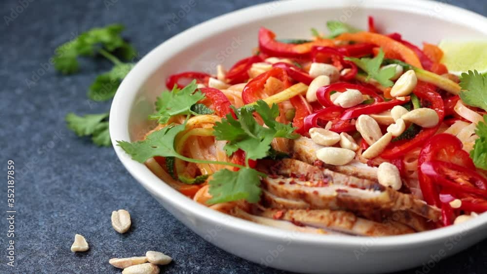 Eating pad thai noodles with chicken, peanuts and vegetables in bowl, dark background. Eating pad thai noodles with chicken, peanuts and vegetables in bowl, dark background.